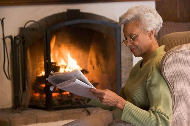 A senior woman keeps warm by the fire (pic - Age UK)